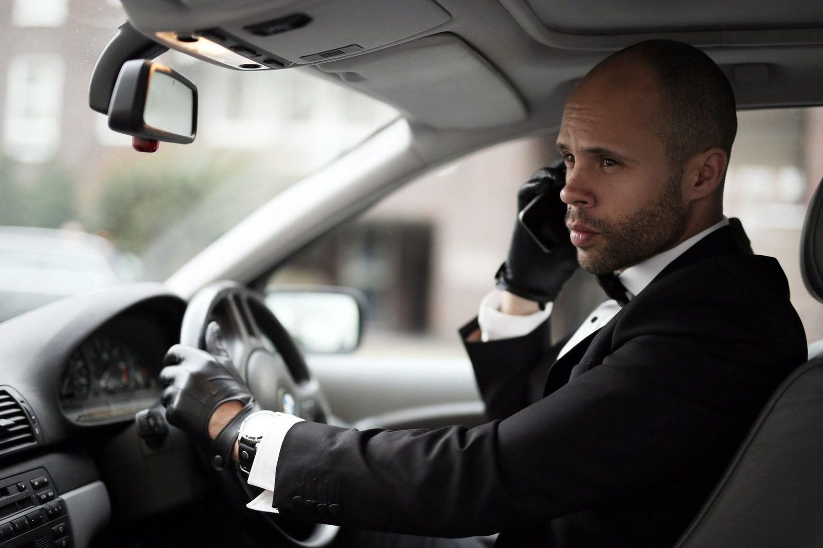 A driver in a suit at the wheel of a luxury car, taking a phone call