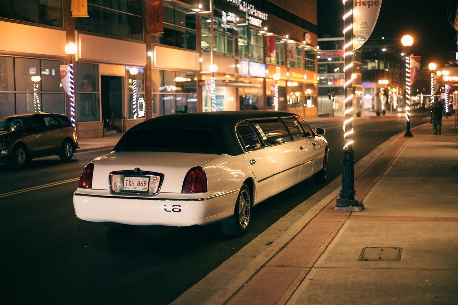 A white stretch limousine parked on a city street at night, lit by shop fronts and street lights